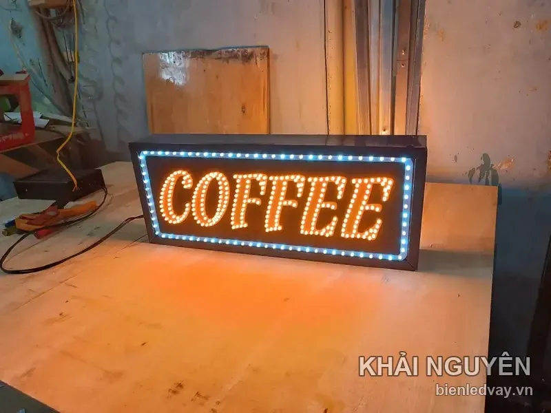 Biển LED chữ COFFEE màu cam, viền bóng trắng xanh, đặt trên bàn tại xưởng