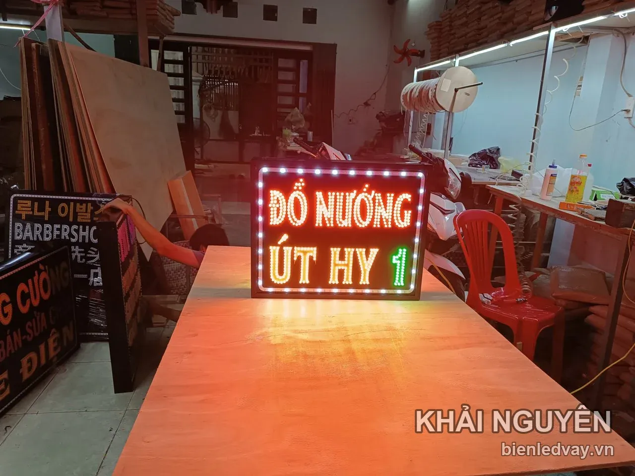 Biển vẫy LED chữ Đồ Nướng đỏ cam và Út Hy vàng, viền bóng trắng, đặt trên bàn gỗ trong xưởng