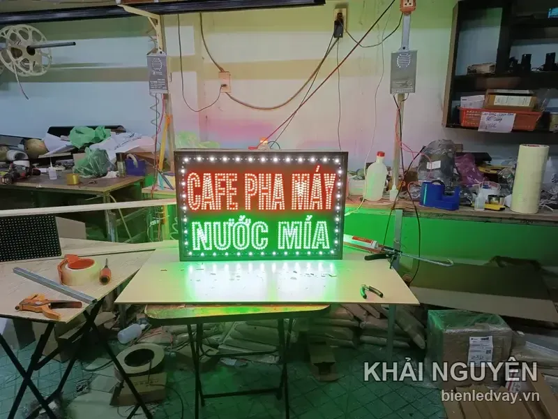 Biển vẫy LED nền đen có viền bóng tròn trắng, gồm chữ CAFE PHA MÁY đỏ và NƯỚC MÍA xanh lá, đang dựng thử trên bàn xưởng.