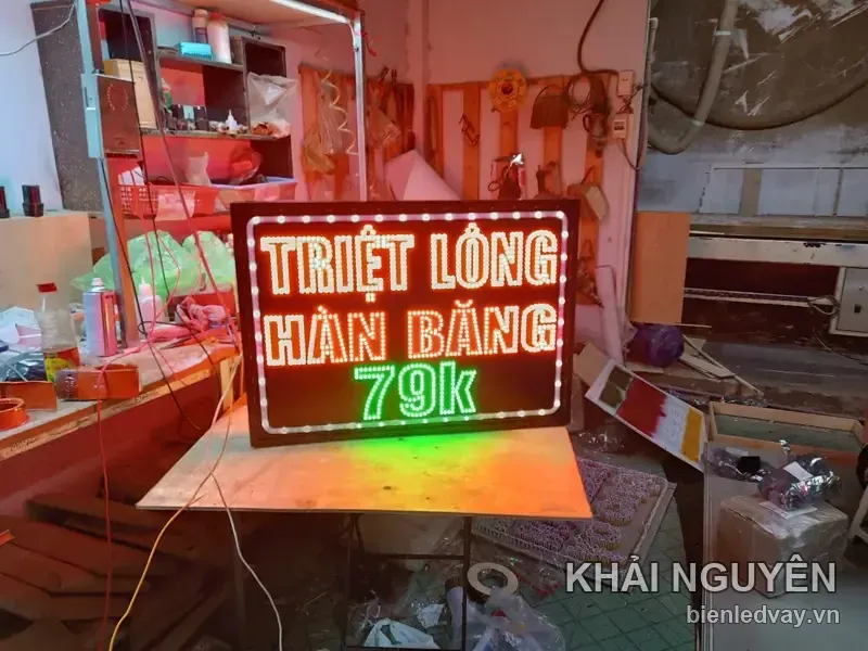 Biển vẫy TRIỆT LÔNG HÀN BĂNG chữ LED vàng trắng, giá 79k màu xanh lá, viền bóng LED trắng, đặt trên bàn gỗ