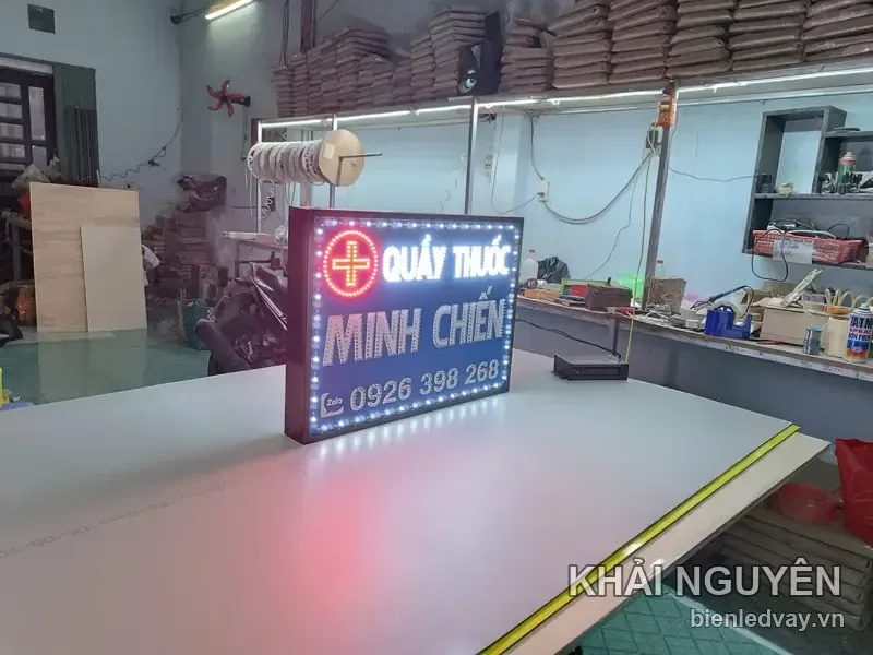 Biển vẫy Quầy Thuốc Minh Chiến nhìn nghiêng trên bàn xưởng, nền tím than, chữ trắng, chữ thập đỏ tròn, viền LED bóng