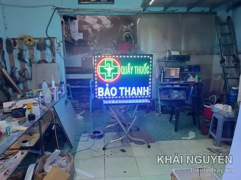 Biển vẫy QUẦY THUỐC BẢO THANH đặt trên chân đế inox giữa xưởng, với tên BẢO THANH xanh dương và chữ thập xanh lá.