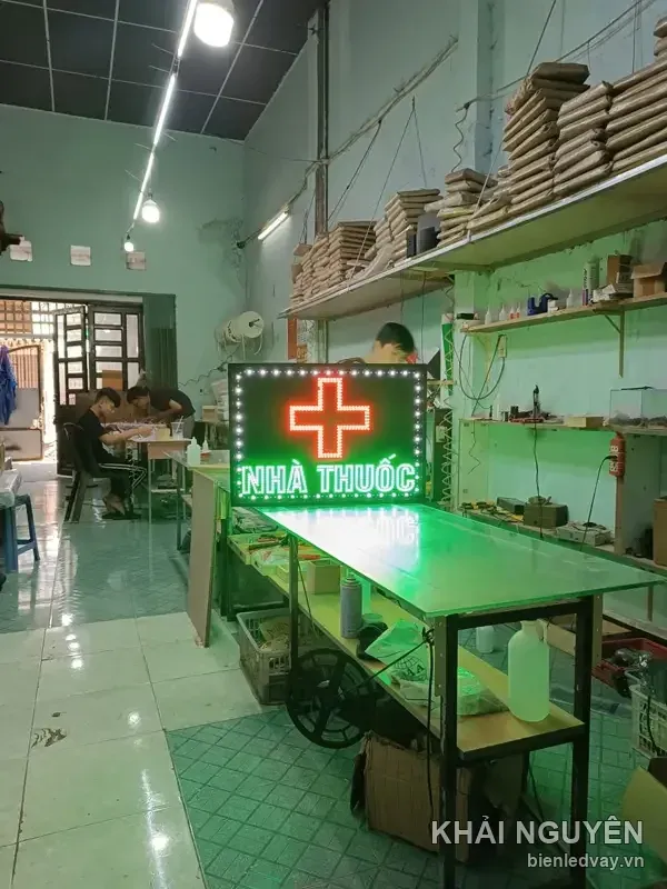 Biển vẫy chữ NHÀ THUỐC đang thử sáng trên bàn xưởng, với chữ xanh lá dưới chữ thập LED đỏ và viền bóng tròn trắng.