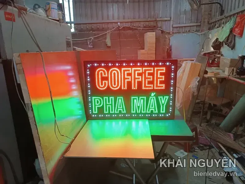 Biển COFFEE PHA MÁY viền LED trắng đặt giữa xưởng trên bàn xếp, phía sau thấy rõ tấm gỗ dựng và mái tôn.