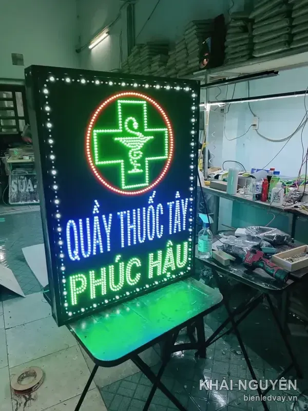 Biển vẫy Phúc Hậu chụp nghiêng trong xưởng, có dòng Quầy Thuốc Tây xanh dương và Phúc Hậu xanh lá