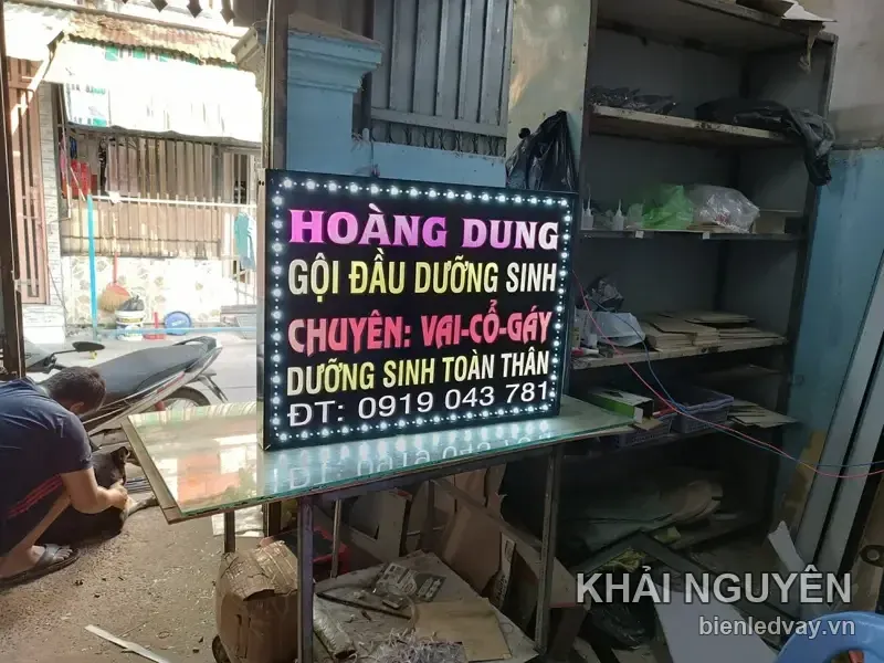 Biển vẫy Hoàng Dung đặt nghiêng trên bàn xưởng, thợ đang làm việc phía sau, chữ LED hồng vàng đỏ trên nền đen