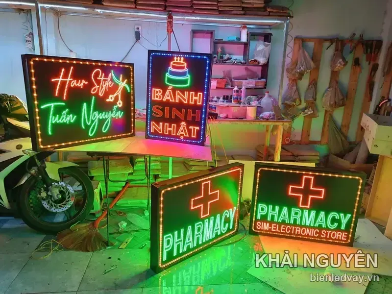 Bốn biển LED dựng sát sàn xưởng cạnh xe máy, hai biển PHARMACY chữ xanh lá, biển tóc và bánh sinh nhật