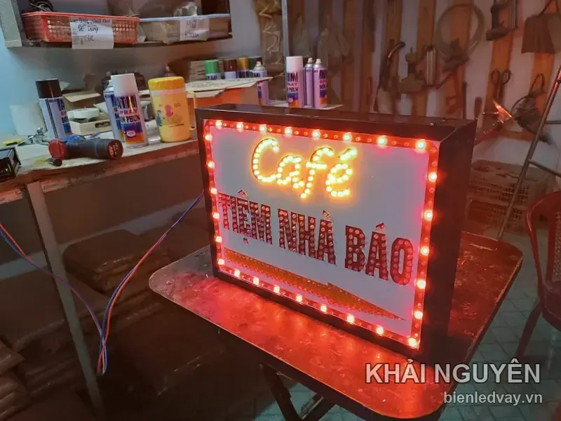 Mặt trước biển vẫy Tiệm Nhà Báo, chữ Café và tên quán ghép từ bóng LED đỏ trên nền trắng, viền màu cam.