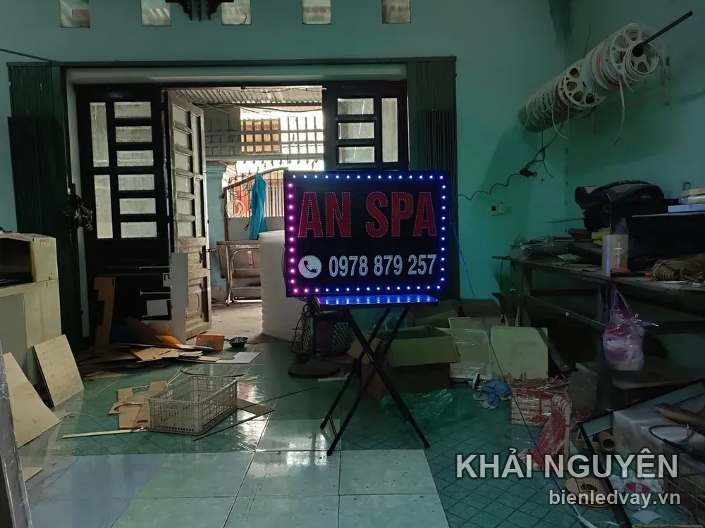 Biển vẫy An Spa chữ LED đỏ trên nền đen, số liên hệ trên biển màu trắng, viền bóng LED xanh tím, đặt trên giá chữ A