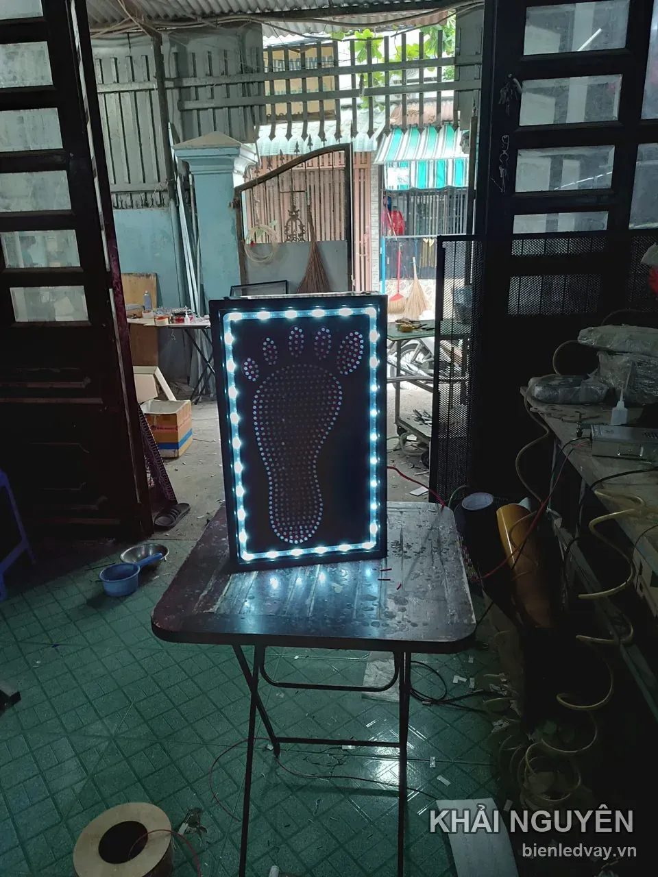 Biển vẫy đặt trên bàn xưởng, phần hình bàn chân ghép bóng LED chưa được cấp điện, chỉ có viền bóng tròn trắng sáng
