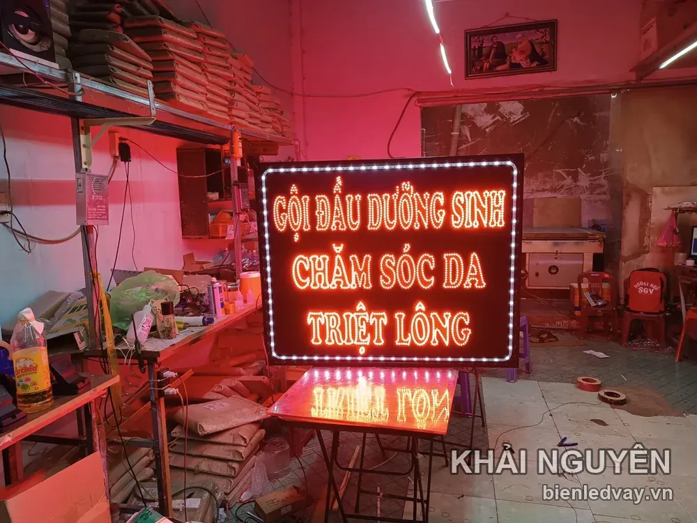 Biển vẫy LED ba dòng gội đầu dưỡng sinh, chăm sóc da, triệt lông đặt trên giá đỡ giữa xưởng, ánh đèn hồng hắt quanh