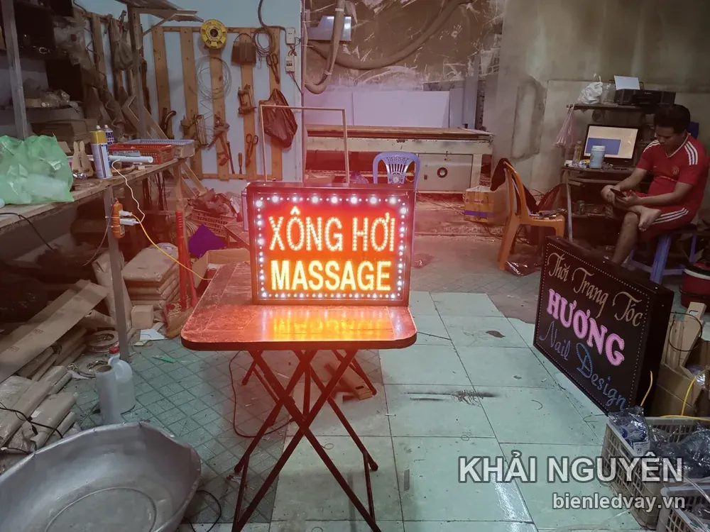 Biển vẫy nền đen chữ bóng LED XÔNG HƠI cam và MASSAGE trắng, viền bóng tròn, đang chạy thử trên bàn xưởng