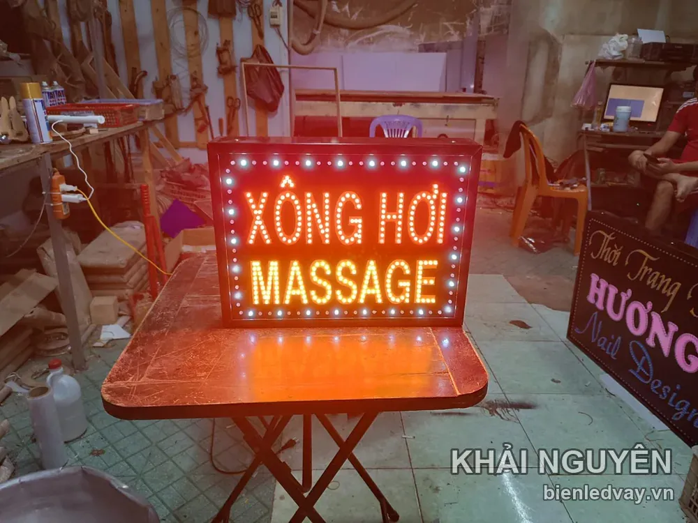 Biển vẫy XÔNG HƠI - MASSAGE nền đỏ, chữ ghép LED cam vàng, viền bóng tròn trắng, đặt trên bàn xưởng