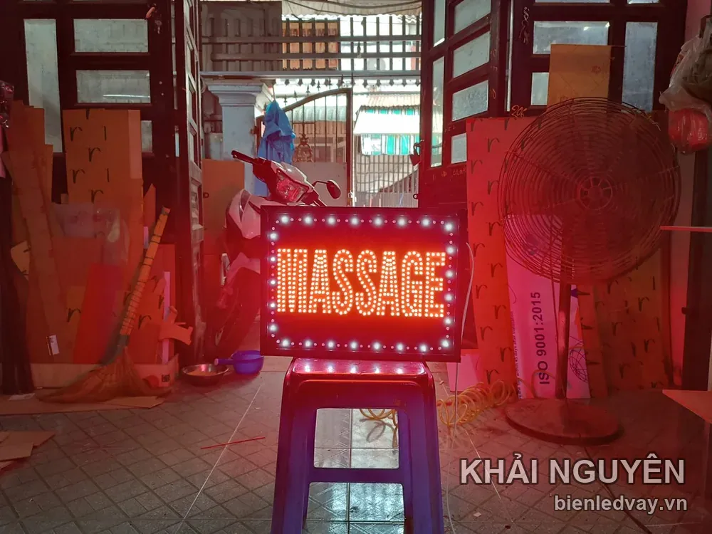 Biển vẫy chữ MASSAGE đỏ trên nền đen, viền LED bóng tròn trắng, đặt thử trên ghế nhựa tại xưởng