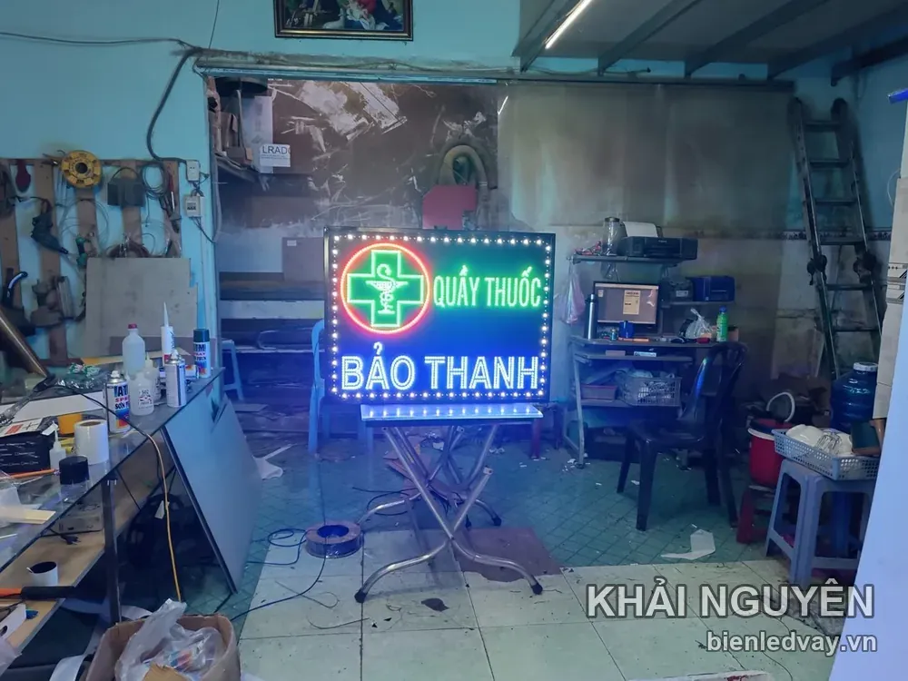 Biển vẫy Quầy Thuốc Bảo Thanh có thập giá xanh trong vòng đỏ, chữ LED trắng, viền bóng vàng và đặt trên bàn xếp