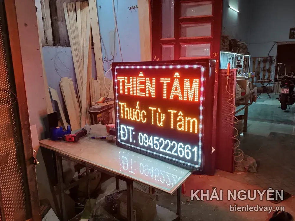 Biển vẫy Thiên Tâm sáng đèn giữa xưởng gỗ, chữ cam đỏ trên nền đen, có số điện thoại trên biển