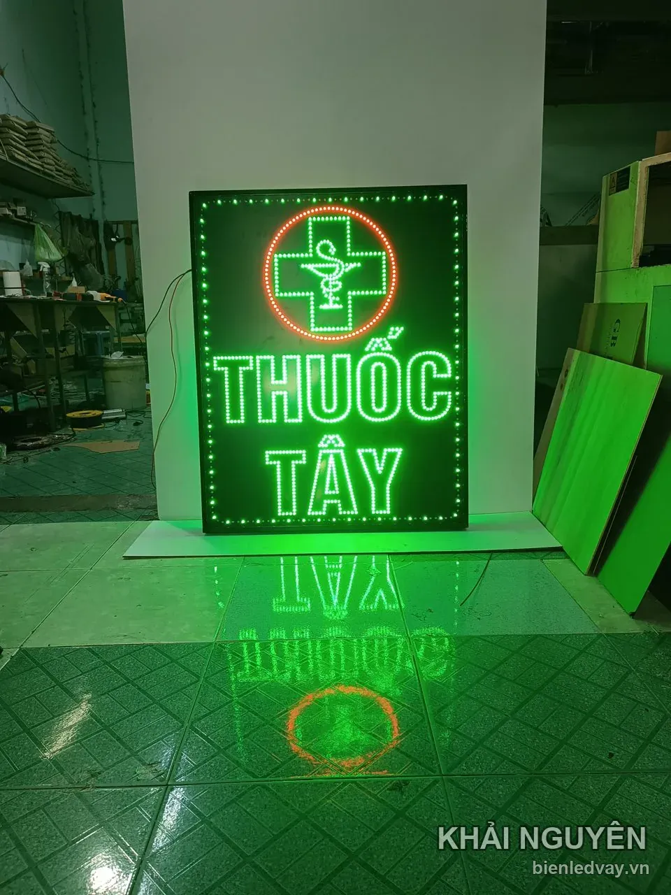 Biển vẫy LED THUỐC TÂY dựng tựa cột trắng, ánh xanh lá hắt loang nền gạch, chữ thập trong vòng tròn đỏ