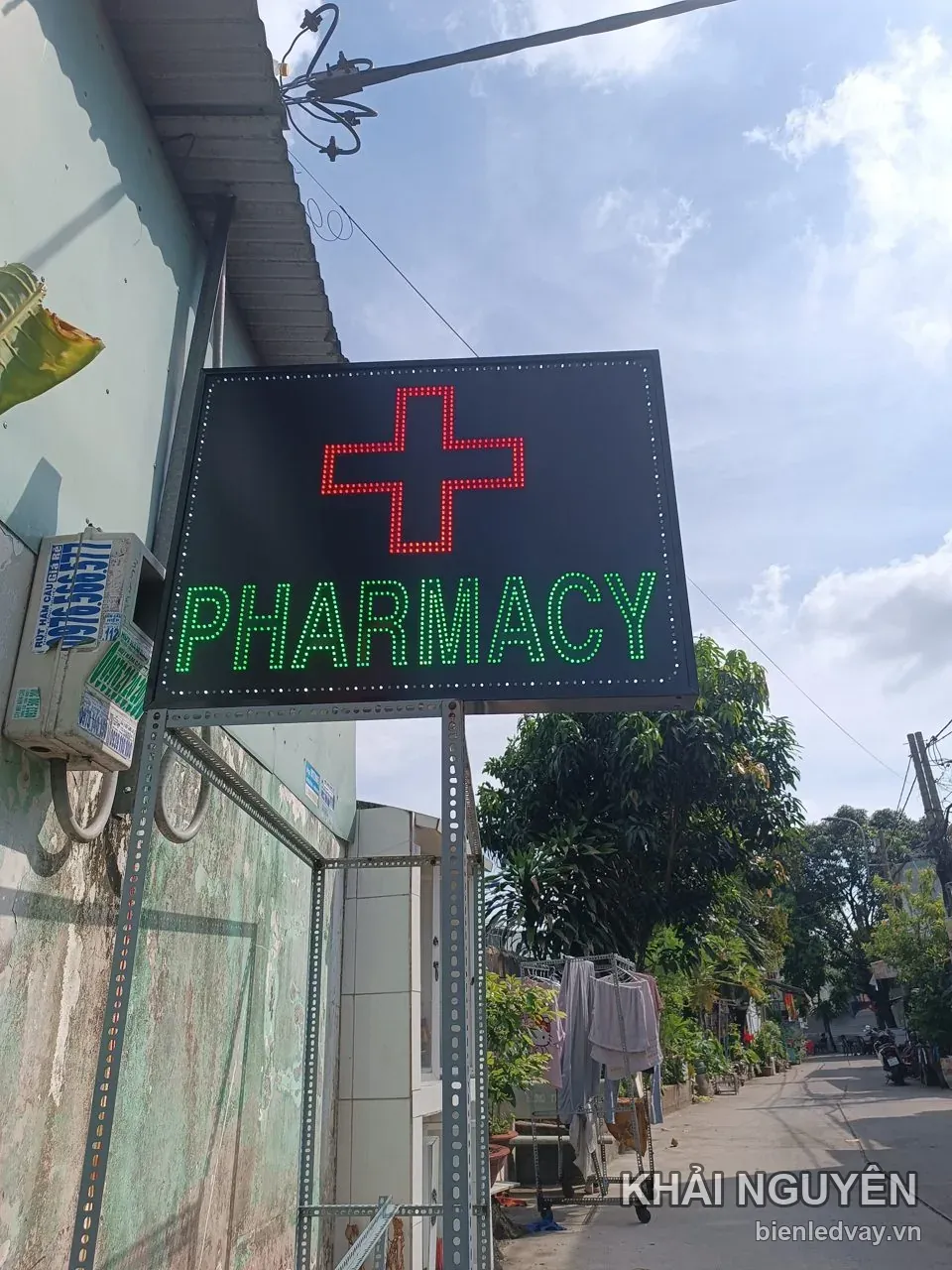 Biển vẫy PHARMACY treo cột thép trước nhà thuốc, chữ thập LED đỏ trên nền đen, chữ xanh lá, viền LED trắng
