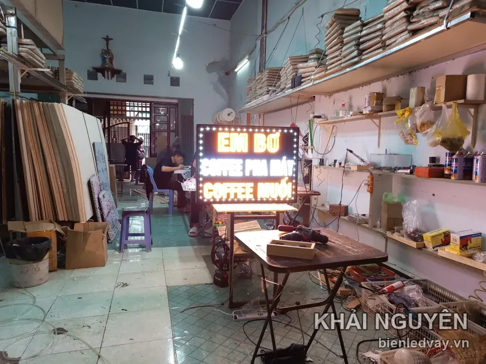 Biển vẫy LED EM BƠ nền đen chữ vàng cam, dòng COFFEE PHA MÁY và COFFEE MUỐI, dựng giữa xưởng cạnh chiếc kệ vật tư
