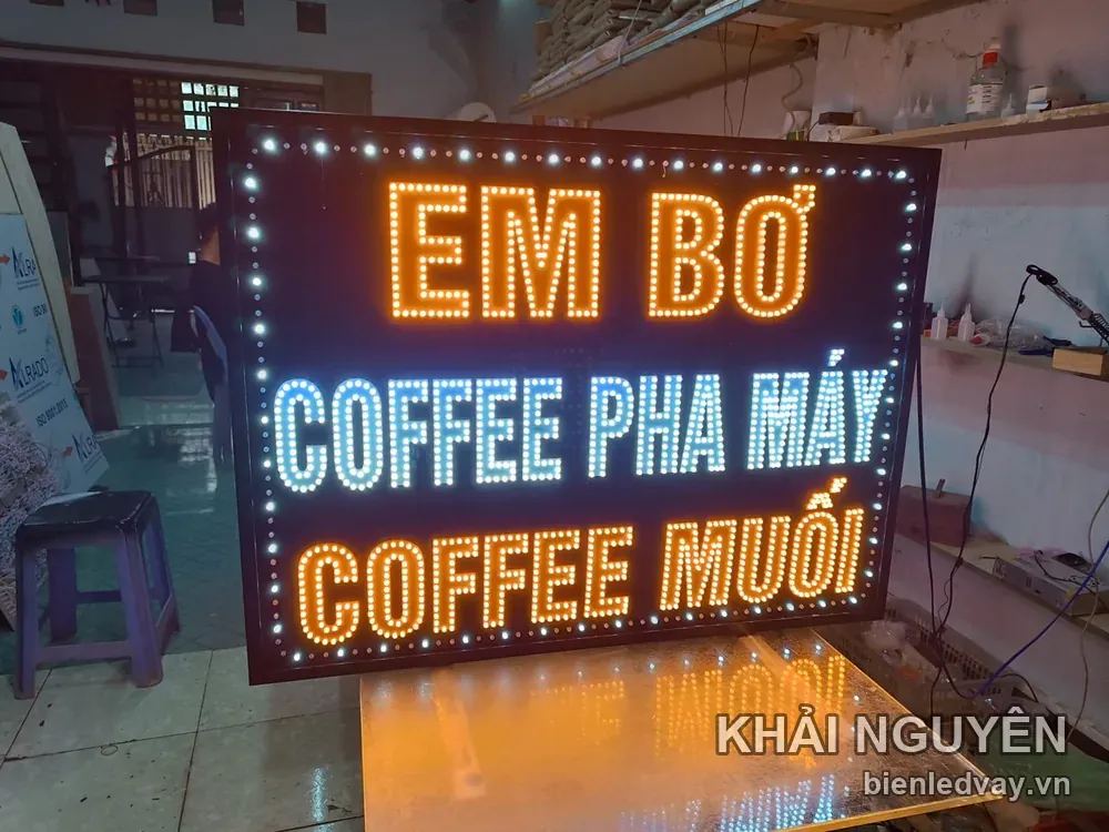 Biển vẫy LED EM BƠ chữ cam, dòng COFFEE PHA MÁY trắng xanh và COFFEE MUỐI cam, viền bóng tròn trên mặt nền đen.