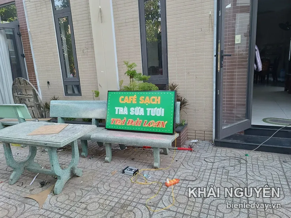 Biển vẫy nền xanh lá CAFÉ SẠCH TRÀ SỮA TƯƠI TRÀ ĐÀI LOAN dựng trên ghế đá trước cửa, đang chạy thử dây điện