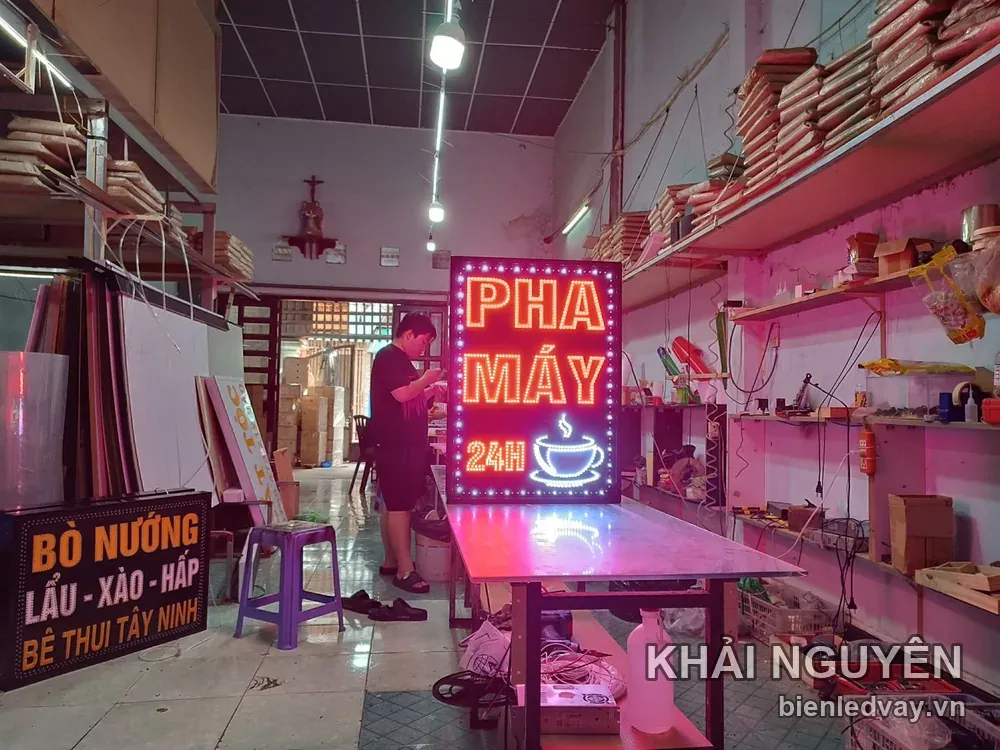 Hình ảnh biển vẫy dọc PHA MÁY 24H LED đỏ viền bóng trắng, kèm hình ly cà phê bốc khói, kê trên bàn inox ở xưởng.