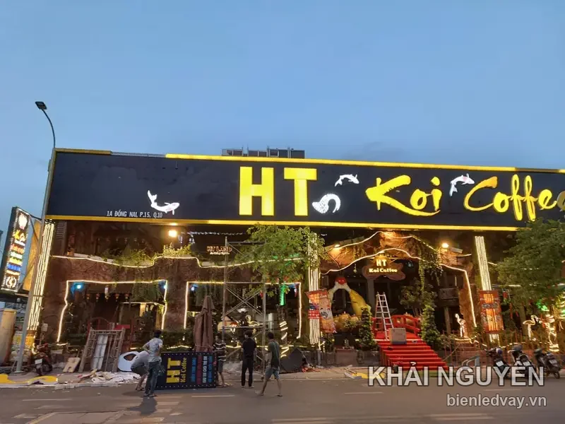 Biển hiệu mặt tiền HT Koi Coffee, chữ nổi vàng cùng hình cá koi trên nền đen, chụp lúc chạng vạng
