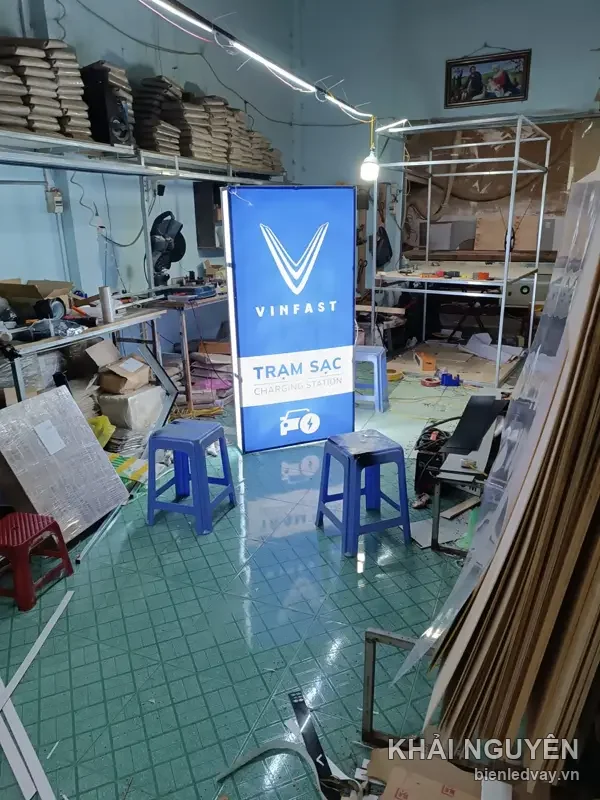 Hộp đèn VinFast Trạm Sạc Charging Station nền xanh dương, logo chữ V trắng, dựng trong xưởng Khải Nguyên