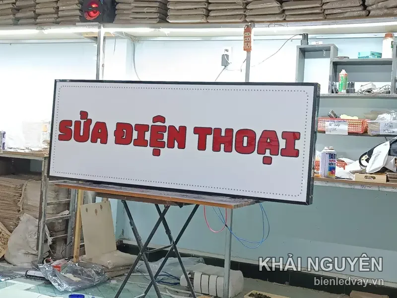 Biển SỬA ĐIỆN THOẠI khổ ngang lúc chưa bật: mặt trắng chữ đỏ, hàng bóng LED viền quanh còn tối, dựng trên giá xếp