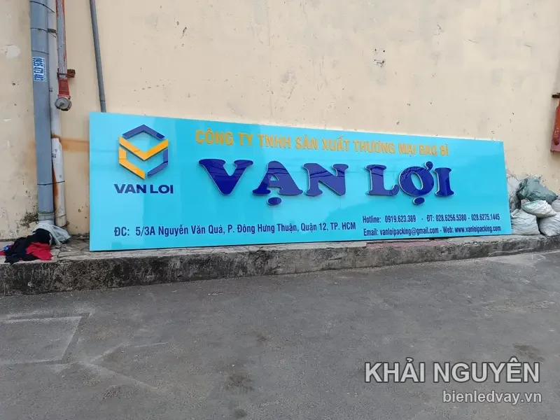 Bảng hiệu alu nền xanh của công ty bao bì Vạn Lợi, chữ nổi VẠN LỢI xanh đậm, logo lục giác vàng, dựng sát tường