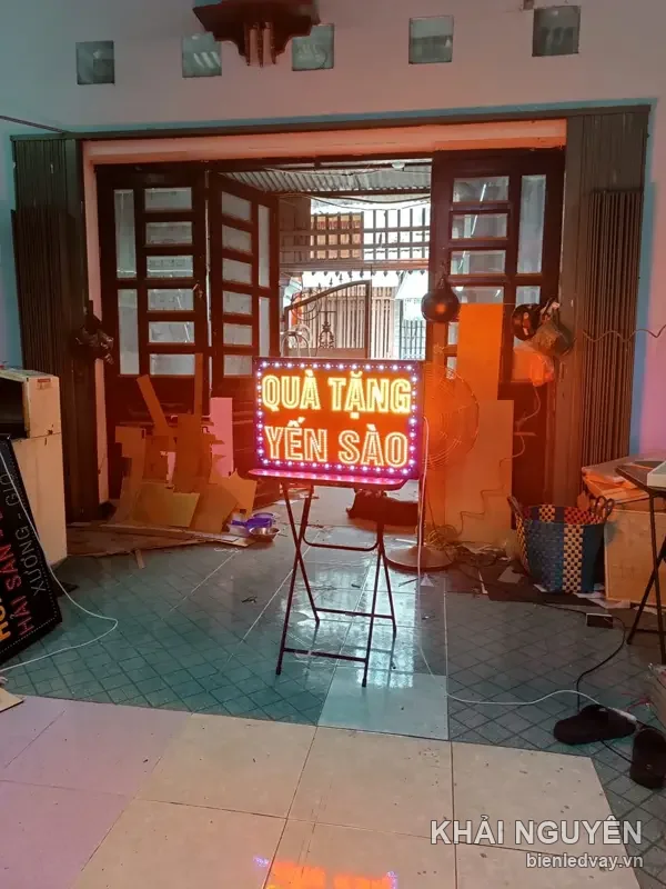 Biển vẫy LED chữ Quà Tặng Yến Sào màu cam hồng, dựng trên chân sắt giữa xưởng đang bật sáng thử