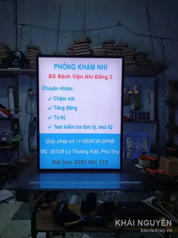 Hộp đèn mica Phòng Khám Nhi nền trắng xanh, liệt kê dịch vụ khám và số đặt hẹn, sáng đèn tại xưởng