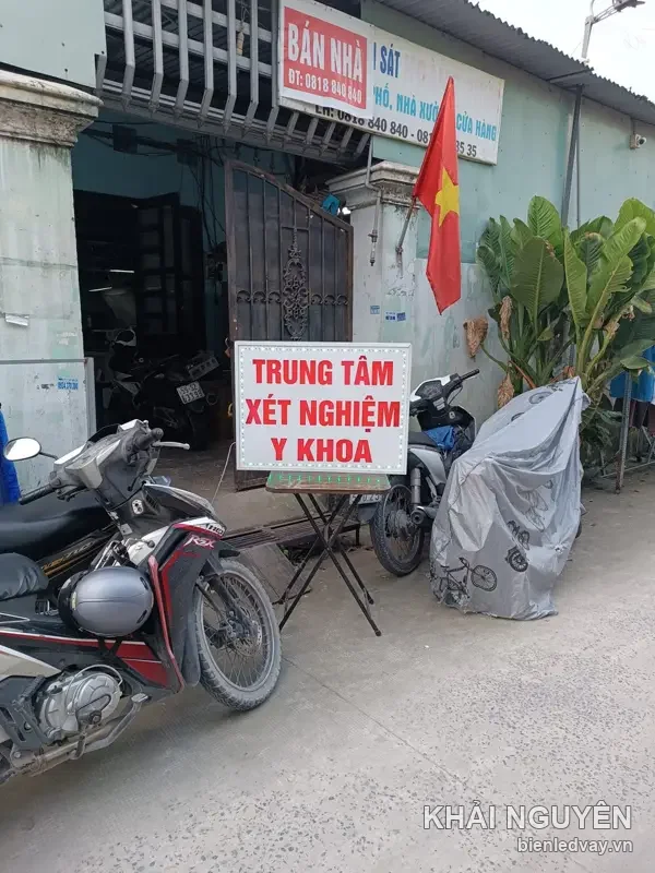 Hộp đèn Trung Tâm Xét Nghiệm Y Khoa nền trắng chữ đỏ, đặt trên bàn xếp trước cửa nhà ngoài phố