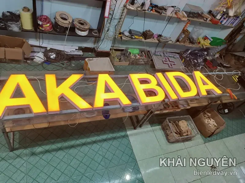 Chữ nổi mica AKABIDA màu vàng cam đang sáng thử trên bàn xưởng, dây điện còn đấu nối lộ ra ngoài