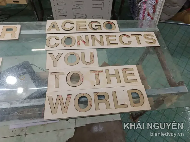Chữ mica ACEGO CONNECTS YOU TO THE WORLD còn nguyên lớp phủ giấy, đặt trên mặt kính xưởng chờ bóc