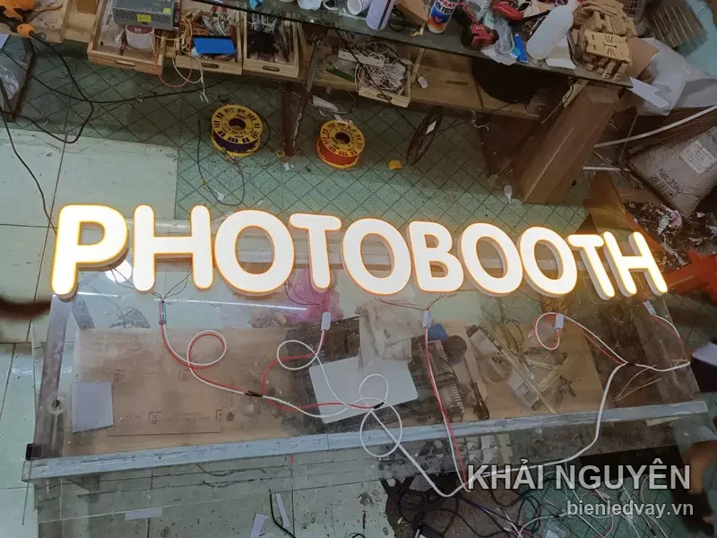 Chữ nổi mica trắng PHOTOBOOTH hắt LED vàng ấm, dây điện còn đấu nối, đặt dưới sàn xưởng khi chạy thử