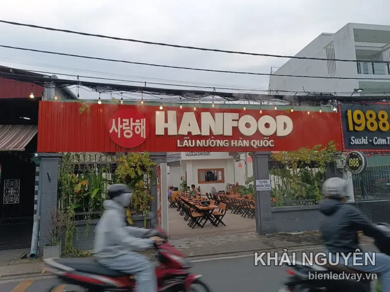 Bảng hiệu hộp đèn HANFOOD nền đỏ chữ trắng nổi, có dòng Lẩu Nướng Hàn Quốc, gắn cao trên mặt tiền quán ven đường