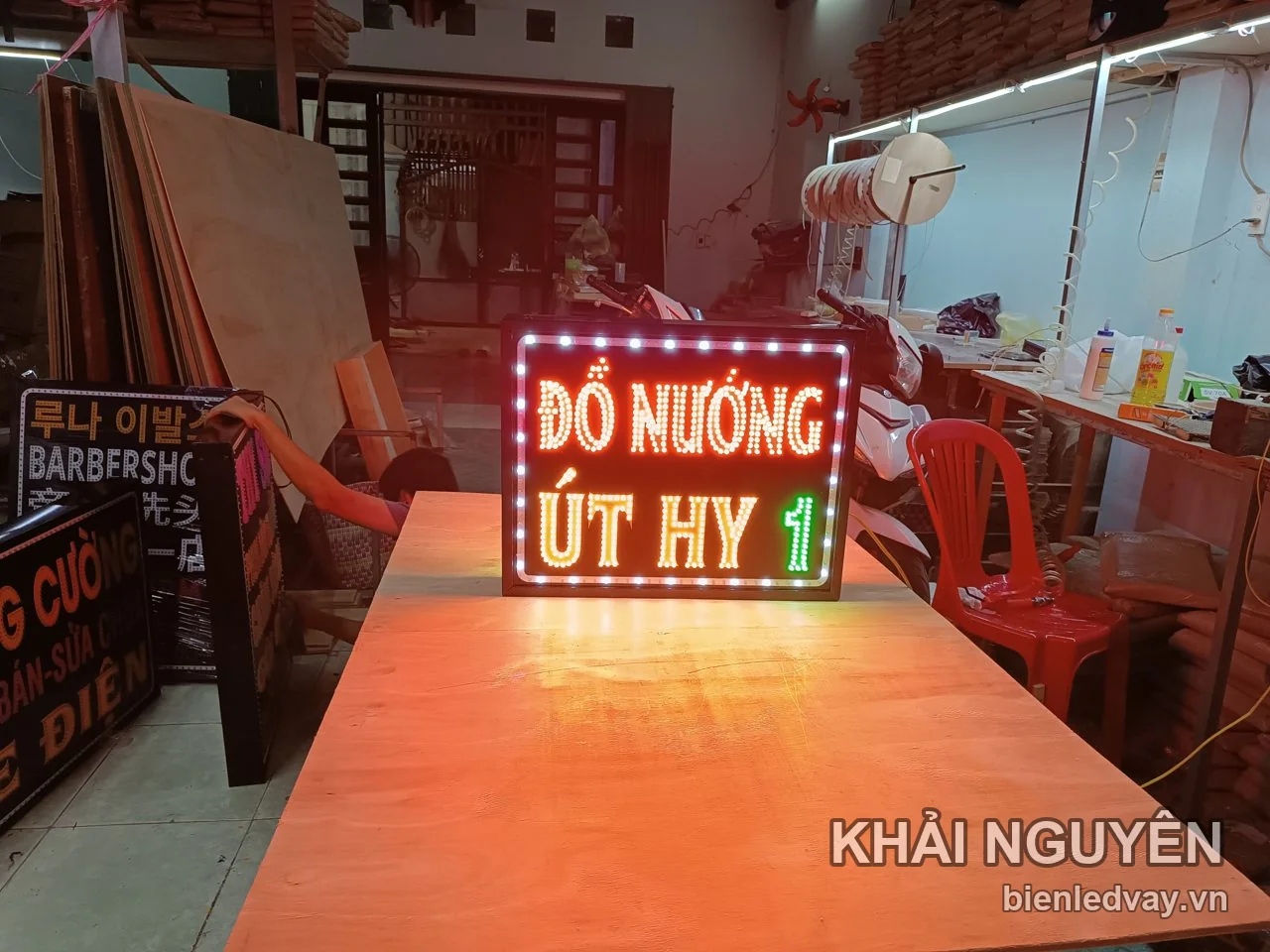 Biển vẫy LED chữ Đồ Nướng đỏ cam và Út Hy vàng, viền bóng trắng, đặt trên bàn gỗ trong xưởng