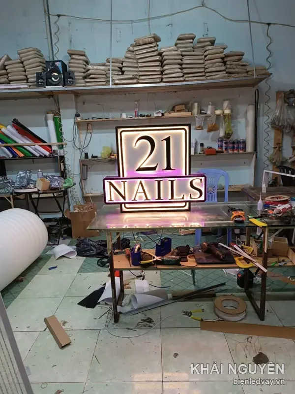 Bảng chữ nổi mica 21 NAILS đèn hắt vàng viền quanh chữ, đặt trên bàn thi công tại xưởng Khải Nguyên