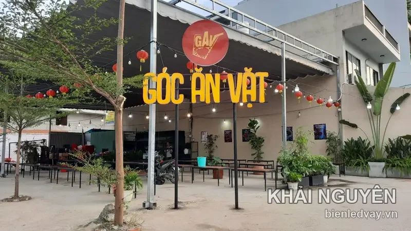 Chữ nổi Góc Ăn Vặt màu vàng cùng logo tròn đỏ GAV gắn trên mái bạt đen, quanh treo đèn lồng đỏ