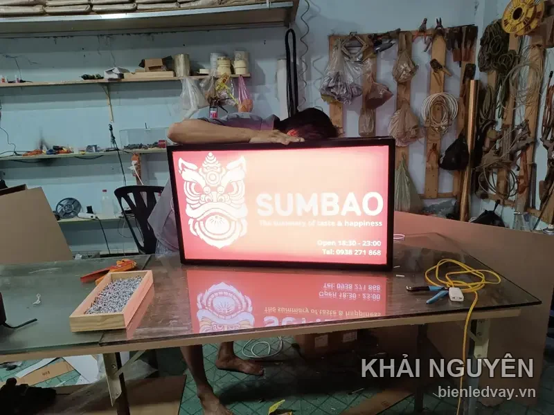 Hộp đèn SUMBAO nền hồng, logo mặt nạ lân trắng, kèm giờ mở cửa 16:30 - 23:00 và số liên hệ trên biển