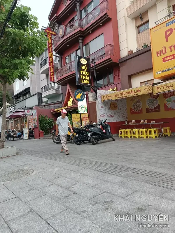 Hộp đèn dọc Pi Thái Hủ Tiếu Thái Lan nền đen chữ vàng treo trước quán, cạnh bạt quảng cáo khổ lớn