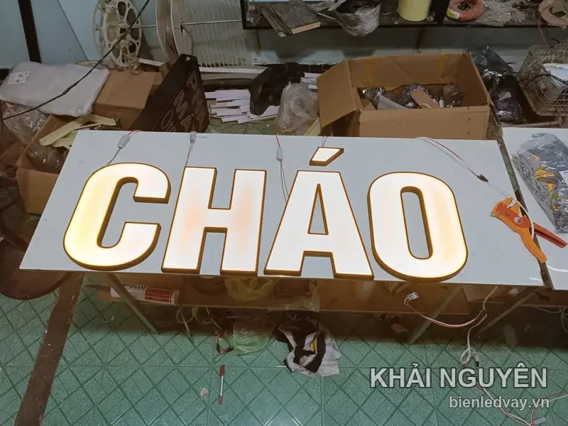 Chữ nổi mica trắng chữ CHÁO hắt sáng vàng ấm, gắn trên tấm nền trắng, đang đấu điện tại xưởng