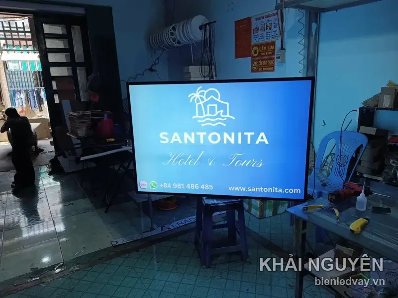 Hộp đèn Santonita Hotel and Tours nền xanh dương, logo ngôi nhà bên biển và chữ trắng, có hotline và website