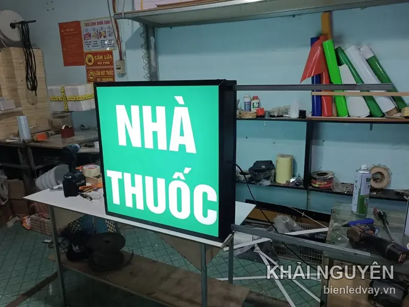 Hộp đèn chữ nhật đứng màu xanh có chữ Nhà Thuốc đang phát sáng tại xưởng