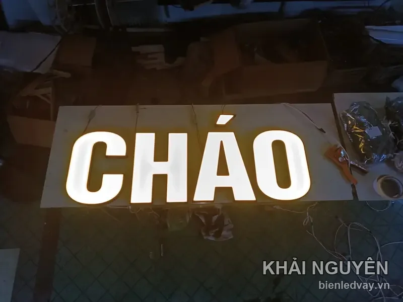 Chữ nổi mica CHÁO màu trắng hắt sáng vàng ấm, đặt trên tấm nền trong xưởng lúc chạy thử đèn