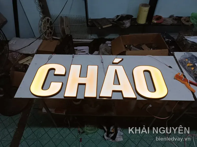 Chữ CHÁO nổi mica trắng hắt sáng vàng ấm, chân chữ còn thò dây điện, xếp thành hàng trên bàn xưởng chờ lắp