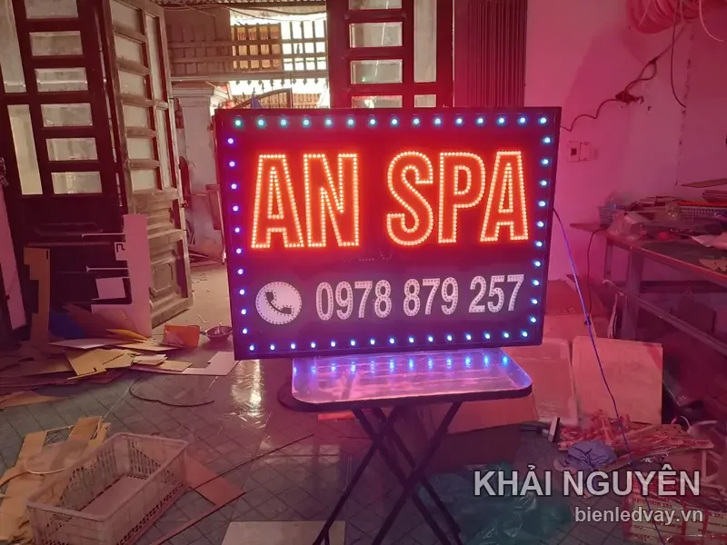 Biển vẫy LED An Spa chữ đỏ cỡ lớn kèm số điện thoại trắng, viền bóng xanh dương, dựng trên bàn tại xưởng