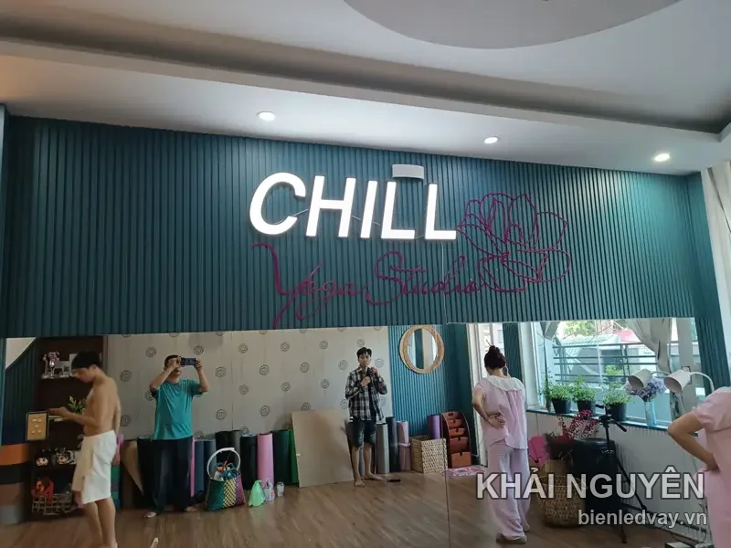 Chữ nổi mica trắng CHILL Yoga Studio trên tường lam gỗ xanh teal, kèm hình hoa và chữ ký màu hồng
