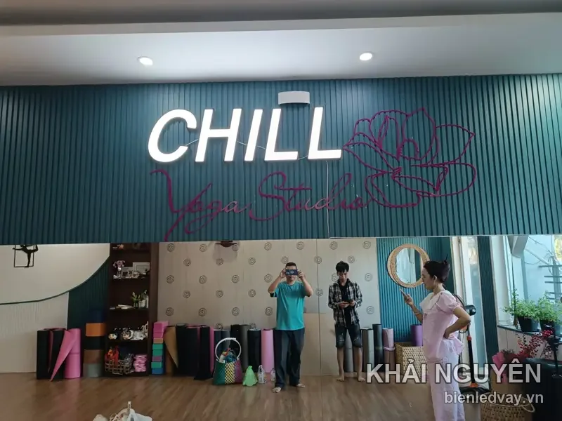 Chữ nổi CHILL trắng phát sáng cùng dòng Yoga Studio và bông hoa neon hồng trên tường sọc xanh teal phòng tập